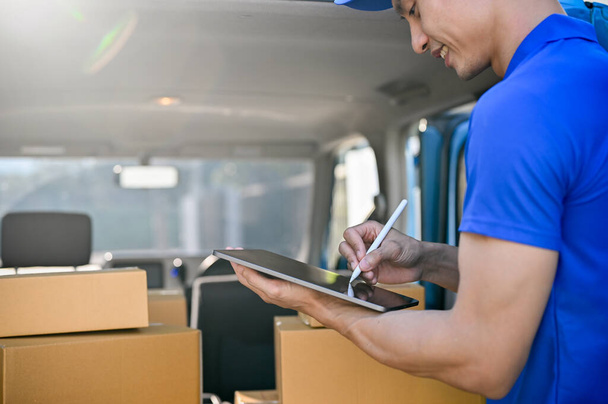 Close up view of delivery man in blue uniform checking package on tablet before sending to the customer. shipping concept - Photo, Image