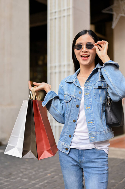 Aziatische vrouw met draagtassen terwijl ze geniet van winkelen in het winkelcentrum. stedelijk leefstijlconcept - Foto, afbeelding