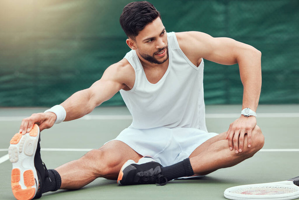 Full length smiling mixed race tennis player stretching legs and getting ready for court game. Hispanic fit athlete sitting alone and holding stretch as warmup before match. Sporty man in sports club. - Photo, Image