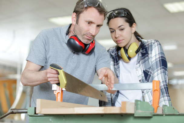 carpenter and apprentice working together in wood workshop - Foto, afbeelding