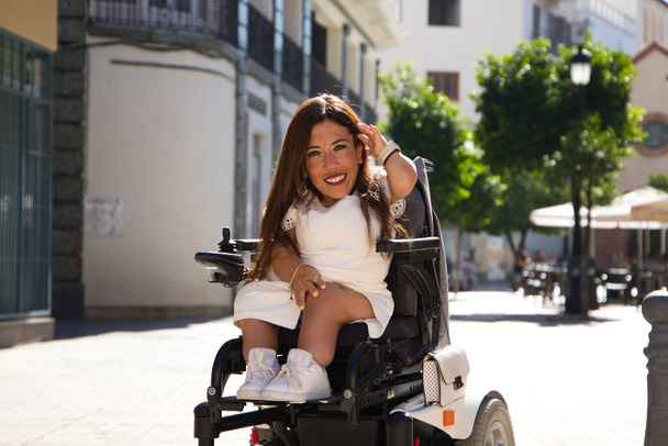 mooie jonge gehandicapte vrouw in rolstoel en beperkte mobiliteit geniet van haar reis door de stad waar ze op vakantie is. - Foto, afbeelding