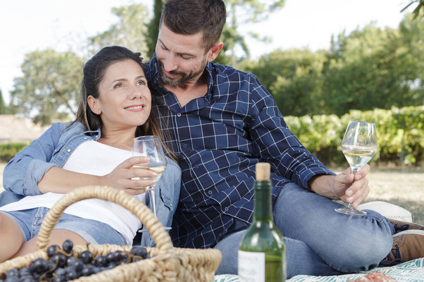 usměvavý šťastný pár odpočívající s vínem venku - Fotografie, Obrázek