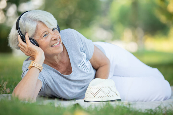 an attractive senior woman using headphones on the grass - Photo, Image