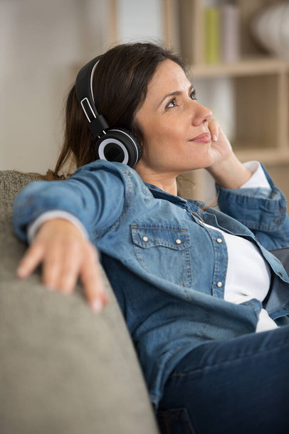 kobieta relaksująca się na kanapie słuchając słuchawek - Zdjęcie, obraz