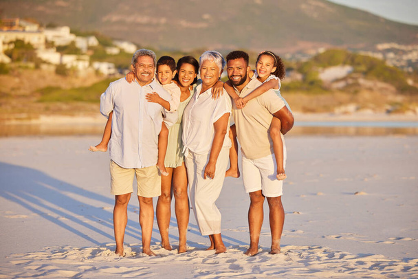 Retrato de larga duración de una familia de varias generaciones de vacaciones de pie juntos en la playa en un día soleado. Familia de raza mixta con dos hijos, dos padres y abuelos pasando tiempo juntos. - Foto, Imagen