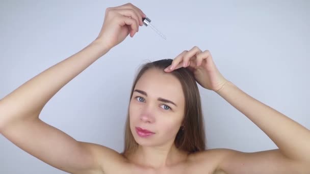 Brunetka dziewczyna nakłada olej na głowę, aby wzmocnić korzenie i dbać o włosy. Środek przeciw łysieniu, kruchości, zbrukaniu, utracie koloru, wzmacnianiu włosów. Koncepcja opieki i kosmetologii - Materiał filmowy, wideo