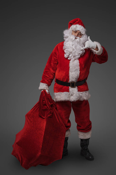 Foto des fröhlichen Weihnachtsmannes in weihnachtsroter Kleidung vor grauem Hintergrund. - Foto, Bild