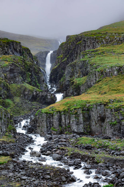 Small waterfall of stream without name snaking through barren mountain side landscape near Reydarfjordur in East Iceland, IS, Europe - 写真・画像
