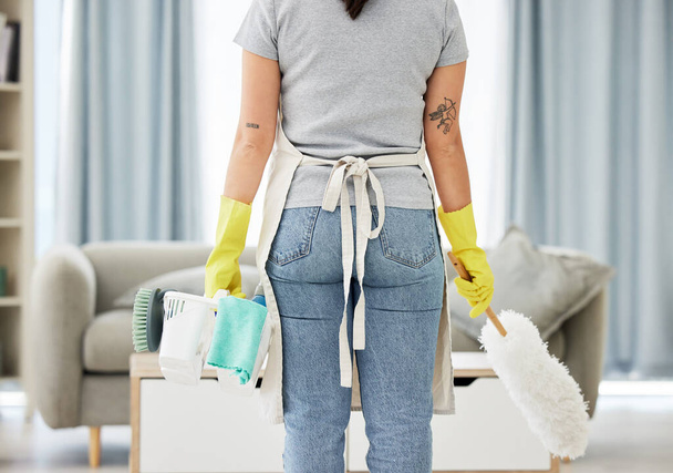 One unknown mixed race woman holding cleaning supplies while cleaning her apartment. An unrecognizable domestic cleaner wearing latex cleaning gloves with a collection of cleaning products. - Fotografie, Obrázek