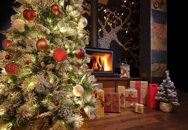 Weihnachtsbaum geschmückt mit traditionellem Weihnachtsschmuck, beleuchtet von Weihnachtslichtern, die mit einem Spiel aus Schatten und Lichtern aufleuchten und Ihnen frohe Weihnachten wünschen. Die schneebedeckten Tannenzweige mit geschmückten Weihnachtskugeln, im Vordergrund - Foto, Bild