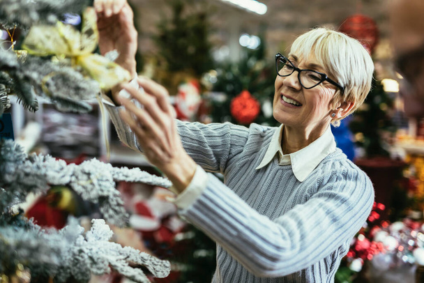 Starsza kobieta na świątecznym targu kupuje zabawki i kulki. Pojęcie świąt Bożego Narodzenia i zakupów noworocznych. - Zdjęcie, obraz