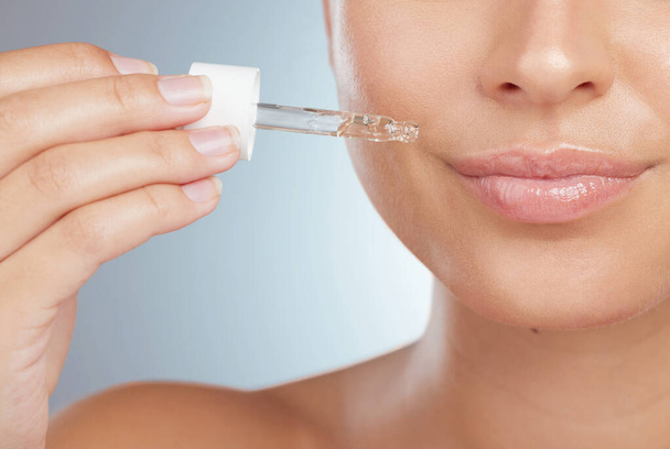 Zbliżenie nieznanej kobiety używającej kroplomierza do nakładania serum na usta. Kaukaski model izolowany na szarym tle w studiu przy użyciu oleju ze skóry dla zdrowego świecącej skóry w rutynie pielęgnacji skóry. - Zdjęcie, obraz