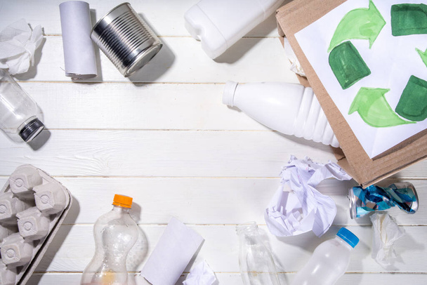 Garbage sorting, waste recycling concept. Box with recycling materials - plastic, glass, paper, cardboard, on white wooden background copy space. Woman hands sorting various rubbish and trash - Foto, imagen