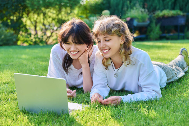 Młode, nastoletnie koleżanki leżące na trawie z laptopem. Nastolatki radujące się razem śmiechem i zabawą. Przyjaźń, Młodzież, Technologia, Szkoła średnia, Szkoła wyższa, Koncepcja stylu życia - Zdjęcie, obraz