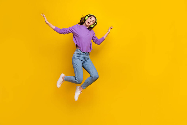 Full size portrait of cheerful delighted girl enjoy favorite music jumping isolated on yellow color background. - 写真・画像