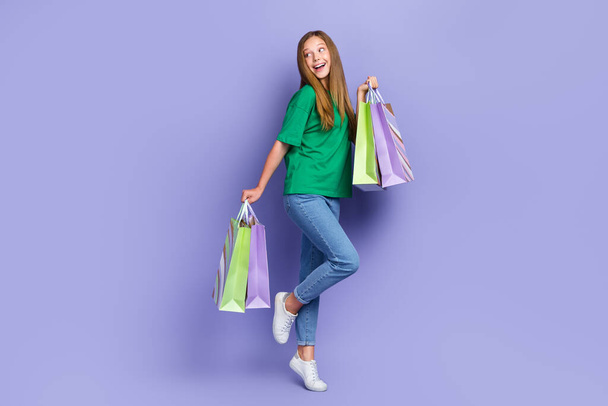 Full length photo of dreamy funny girl dressed green t-shirt holding bargains looking empty space isolated purple color background. - Φωτογραφία, εικόνα
