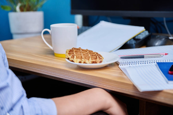 Female teenager sits at home at the table studying, snacking on waffles, drinking tea - Foto, immagini