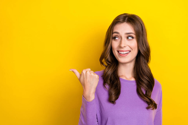 Photo of sweet pretty girl dressed purple pullover looking pointing thumb empty space isolated yellow color background. - Φωτογραφία, εικόνα