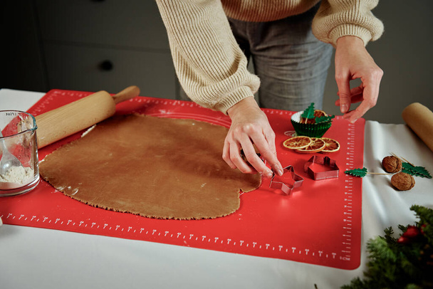 Female hands cutting figures from ginger dough with cutter. Cooking gingerbread cookies to preparing for winter holidays. Christmas baking - Photo, Image