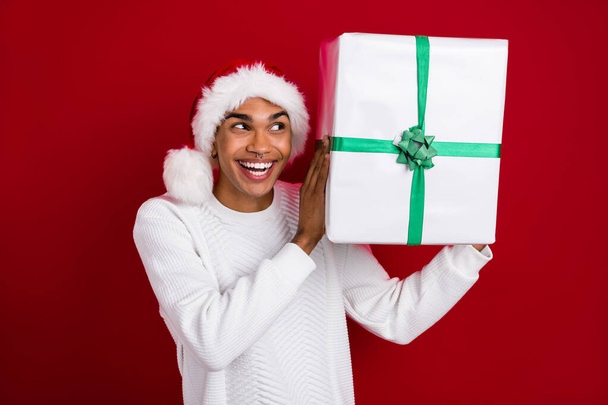 Photo of funky santa claus excited man wear white pullover hold christmas gift shaking guess what inside isolated on bright red color background. - Foto, Imagen