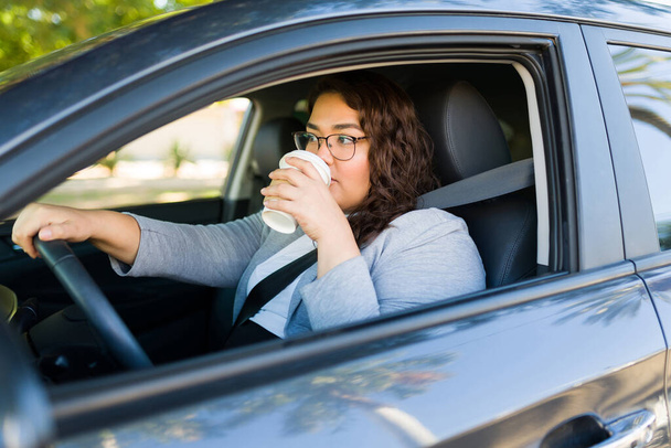 İspanyol çekici obez kadın sabah işe giderken gidip arabasını sürmek için kahve içiyor. - Fotoğraf, Görsel