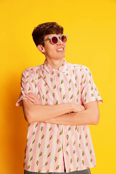 Sommerurlaubsstimmung. Porträt eines erstaunten jungen Mannes in modischer Brille, der isoliert auf leuchtend gelbem Hintergrund lächelt. Jugendkultur, positive Emotionen. Sieht aufgeregt, erfreut aus - Foto, Bild