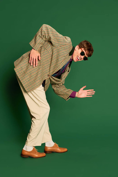 Studio footage young man in vintage fashion style costume, suit posing isolated on dark green background. Concept of retro style, creativity, emotions, facial expression, fashion and business - Photo, Image