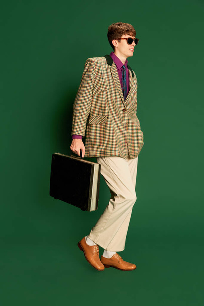 Hipster. Studio footage young man in vintage fashion style costume, suit posing isolated on dark green background. Concept of retro style, creativity, emotions, facial expression, fashion and business - Foto, afbeelding