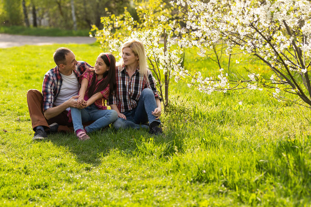 Gelukkig ouders mam en pap, dochter, jong gezin buiten in het voorjaar tegen de achtergrond van bloeiende appel en kersenbomen. - Foto, afbeelding