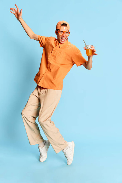 Hiphop. Portret van jonge emotionele man in casual kleding en pet geïsoleerd over lichtblauwe achtergrond. Concept van gevoelens, jeugd, mode, gezichtsuitdrukking, emoties, levensstijl, reclame - Foto, afbeelding