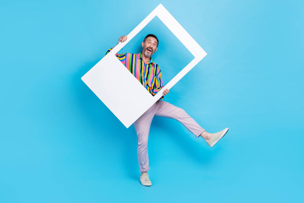 Full length photo of cheerful positive man wear vintage stylish outfit have fun hold white frame picture isolated on blue color background. - Foto, Imagen