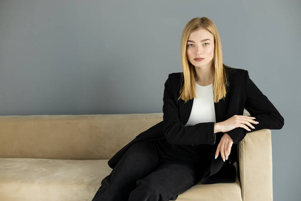 Portrait of young woman in jacket sitting on couch and looking at camera  - Foto, imagen