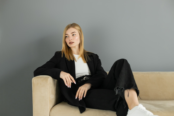 Bella donna in giacca guardando lontano mentre seduto sul divano a casa  - Foto, immagini
