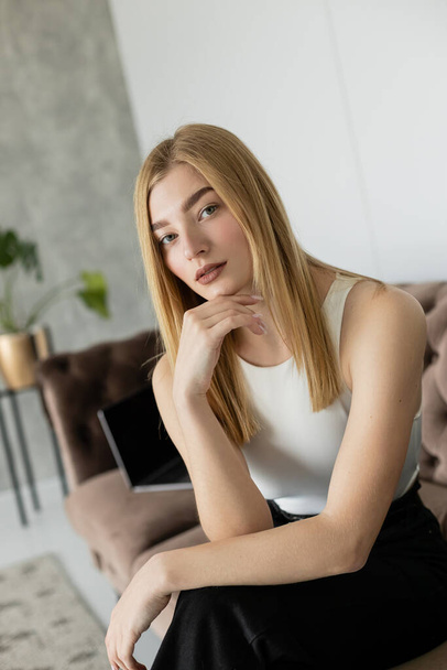 Portrait of young woman looking at camera while sitting on blurred couch at home  - Foto, afbeelding