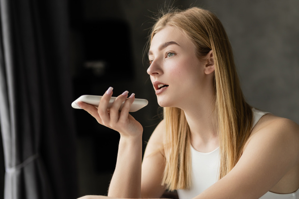 Blonde woman recording voice message on smartphone at home  - Photo, Image