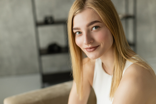 Porträt einer blonden jungen Frau, die zu Hause in die Kamera lächelt  - Foto, Bild