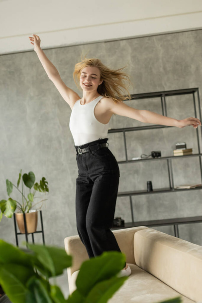 excited woman with closed eyes and outstretched hands dancing on sofa at home - Photo, Image