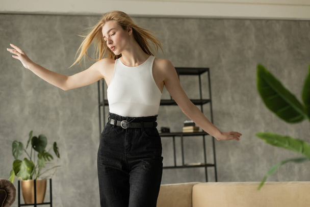 blonde woman with outstretched hands pouting lips while dancing at home - Valokuva, kuva