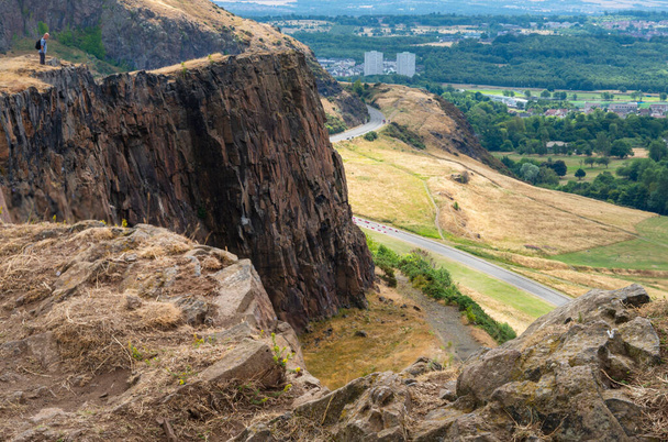 Looking down to pathways of Holyrood Park far below.narrow paths across sheer vertical cliff faces,dramatic views across the Scottish capital city,on a summer day. - Foto, immagini