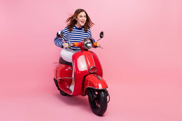 Full size portrait of cheerful pretty girl driving scooter empty space isolated on pink color background. - Foto, Imagem