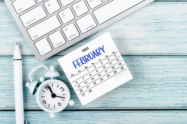 febbraio 2023 Anno solare mensile e sveglia con computer a tastiera su sfondo blu in legno. - Foto, immagini