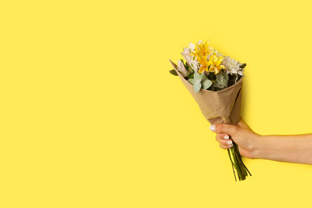 Woman hand holding a yellow and white flowers bouquet on a yellow background with copy space - Photo, image