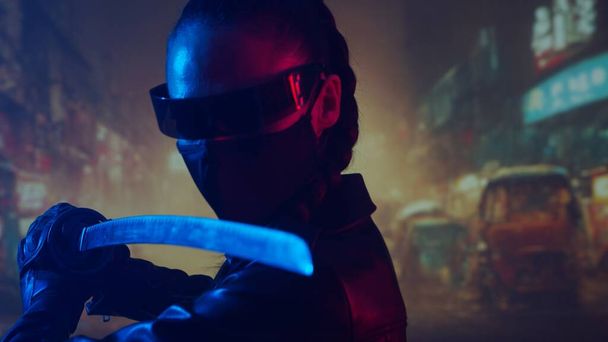 Cyberpunk ninja girl in a mask and with a katana. Beautiful female samurai woman on the background of Asian city downtown street. - Photo, image