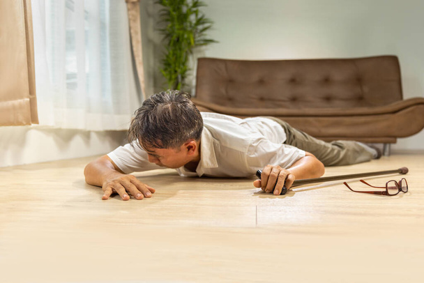 Asijské senior muž padající a ležící na podlaze při chůzi s vycházkovou holí doma. - Fotografie, Obrázek