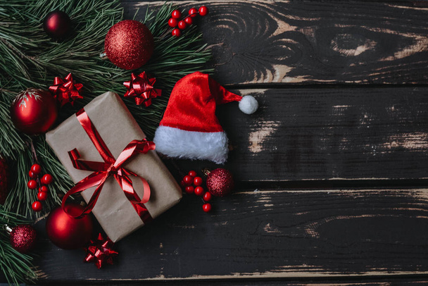 Widok z góry zdjęcie Christmass flatlay prezent pudełko, czerwone zabawki choinkowe, Santa kapelusz i świerk brance na drewnianym tle. Tło świąteczne z miejscem na tekst. Copyspace. - Zdjęcie, obraz