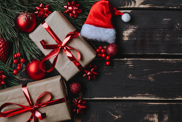 Top view zdjęcie Christmass flatlay pudełka prezentów, czerwone zabawki choinkowe, Santa kapelusz i świerk brance na drewnianym tle. Tło świąteczne z miejscem na tekst. Copyspace. - Zdjęcie, obraz