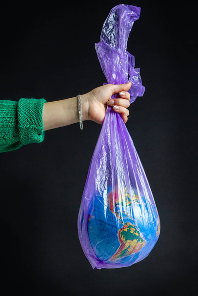 Female hand holding plastic bag with world globe. Isolated on black background. - Foto, Imagem