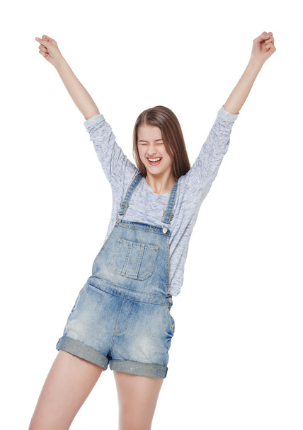 Happy young fashion girl in jeans overalls with hands up isolate - Valokuva, kuva
