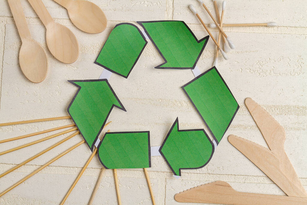 Top view recyclig symbool en houten gebruiksvoorwerpen. Lepels met messen en oorstokjes. - Foto, afbeelding