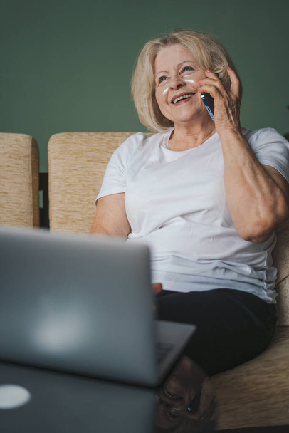 Szczęśliwa, dojrzała emerytka relaksuje się sama na wygodnej sofie, rozmawiając przez telefon komórkowy, spędzając weekend sama w domu. Pokolenie osób starszych - Zdjęcie, obraz